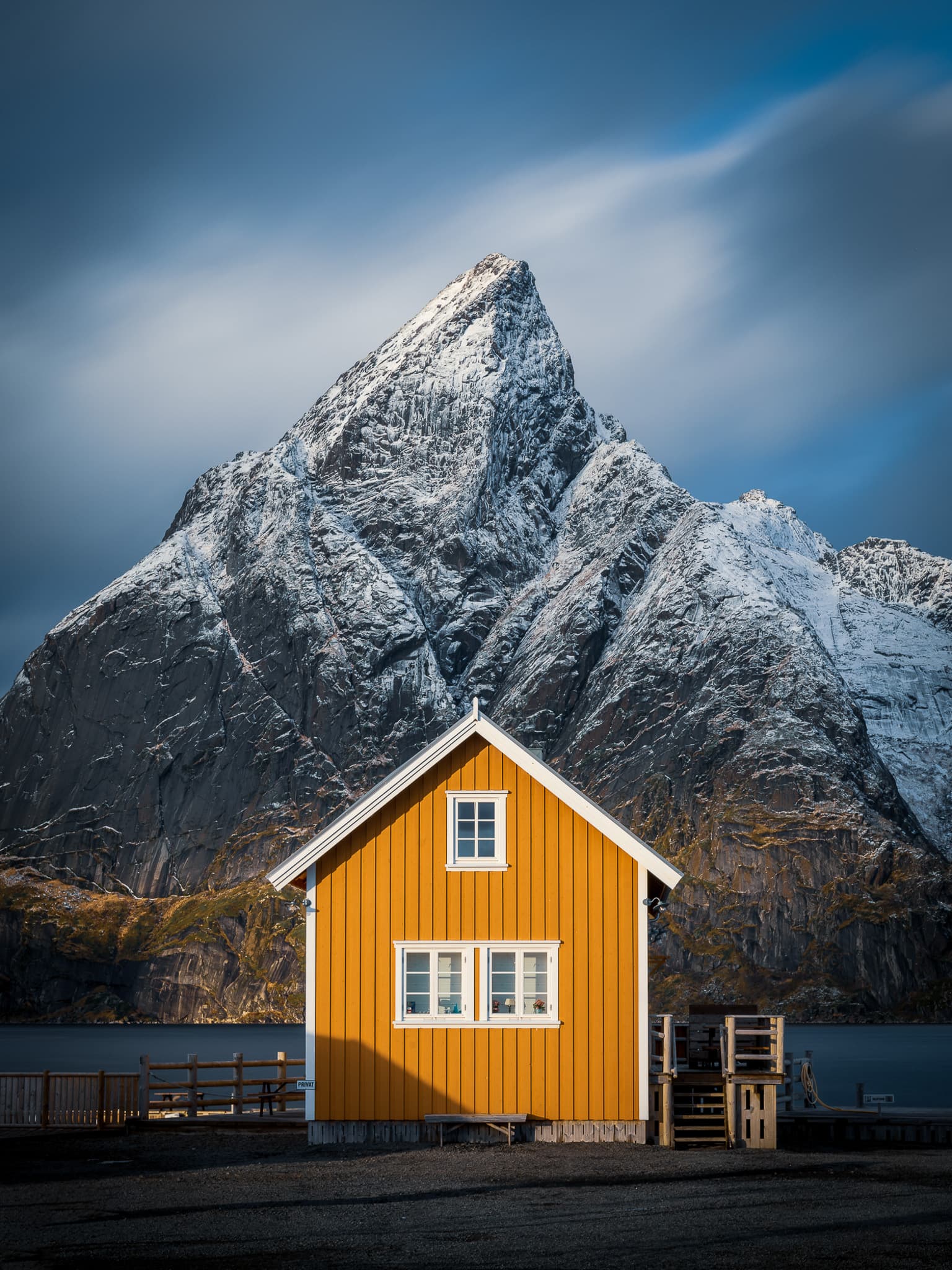 A yellow Norwegian house framed beneath a snow-covered mountain, photographed by Mohammad Anabtawi