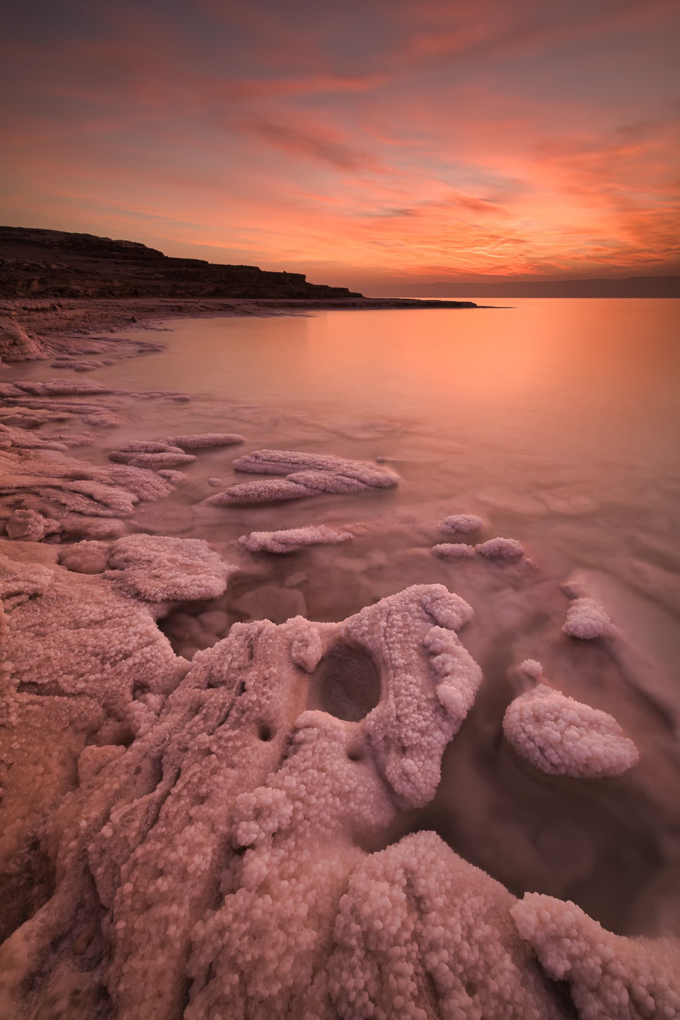 Salt formations along calm water beneath a vivid coral sunset