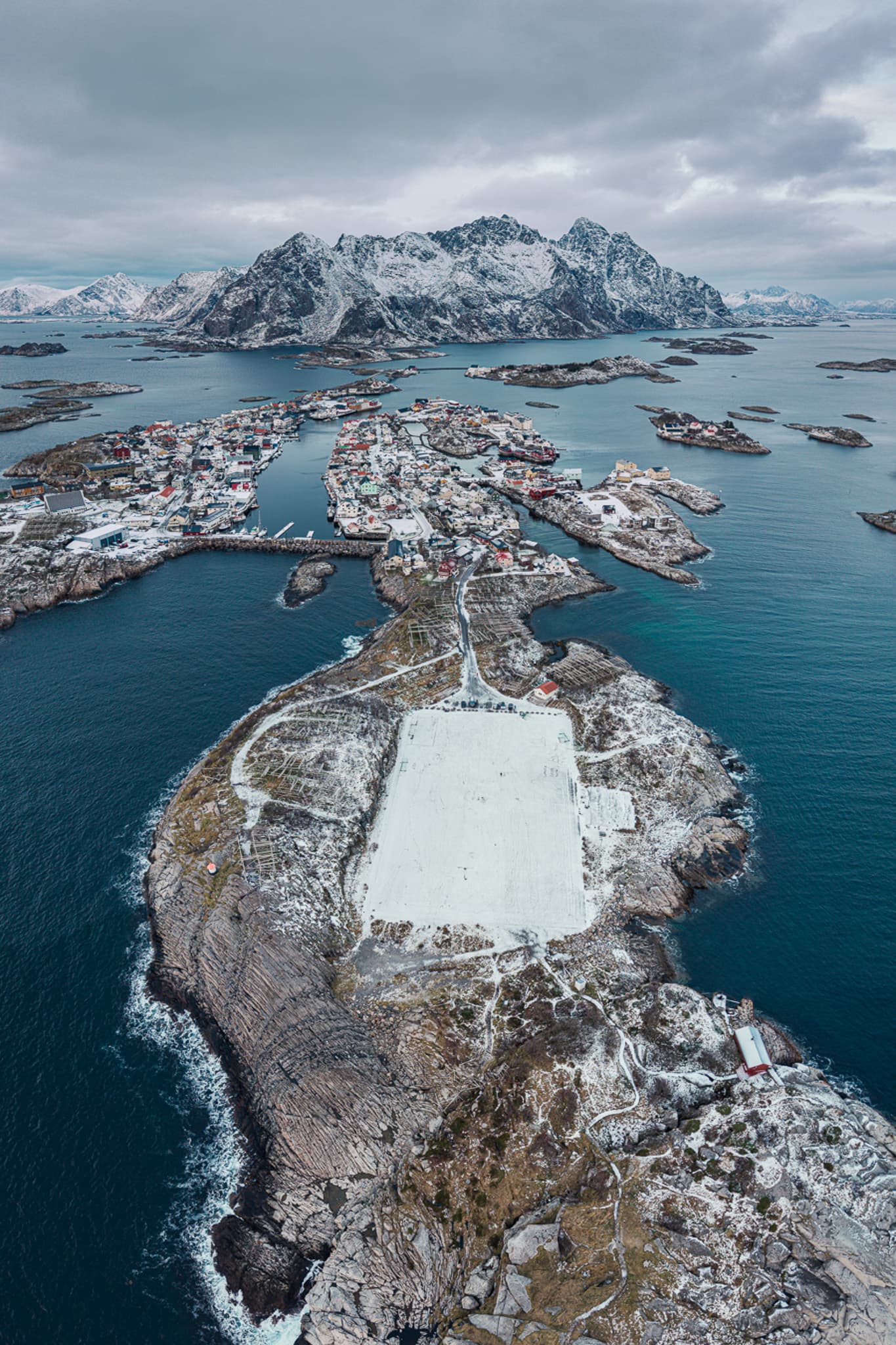 Aerial view of a snow-covered Norwegian fishing village surrounded by sea and mountains