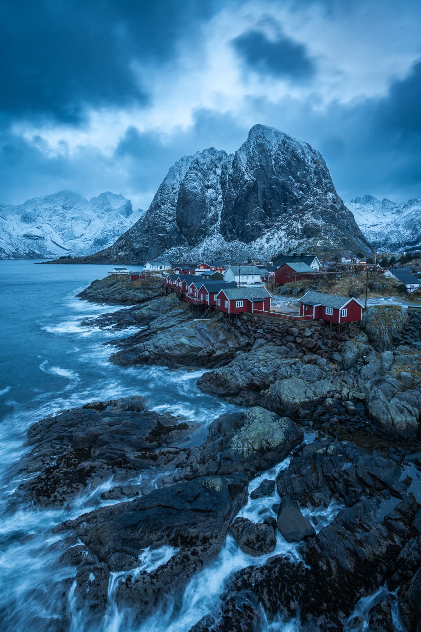 Red fishing cabins beneath a snow-dusted mountain on the Norwegian coast